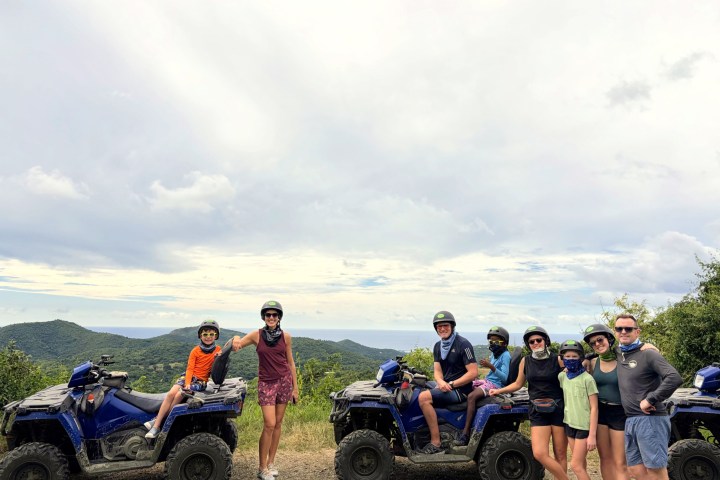 Group of people with ATVs on a mountain trail under a cloudy sky.