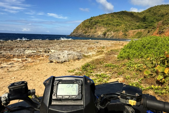 ATV dashboard view on rocky beach with ocean and hill.