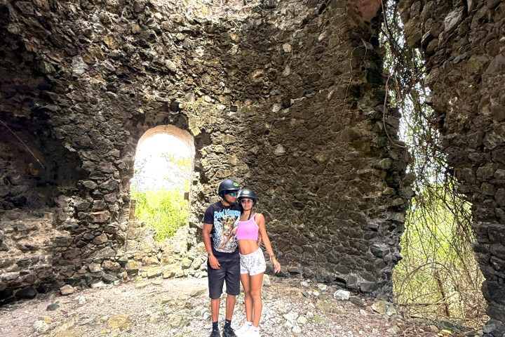 Two people in helmets inside a stone ruin with an arched doorway.